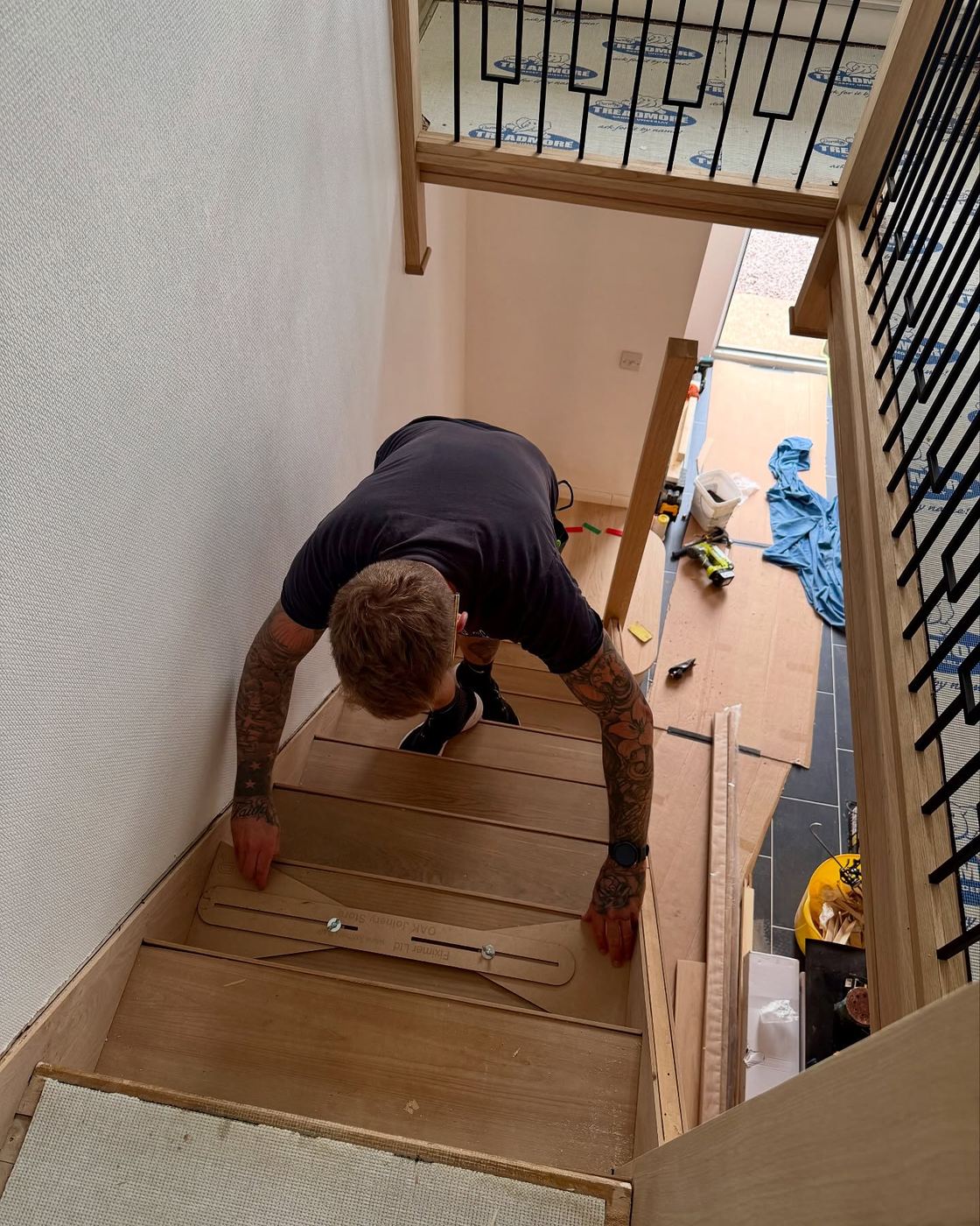 The joiner kneeling on a part-built oak staircase, setting a tread into position